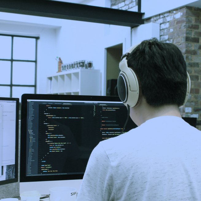 A person wearing headphones is looking at a computer screen displaying lines of code