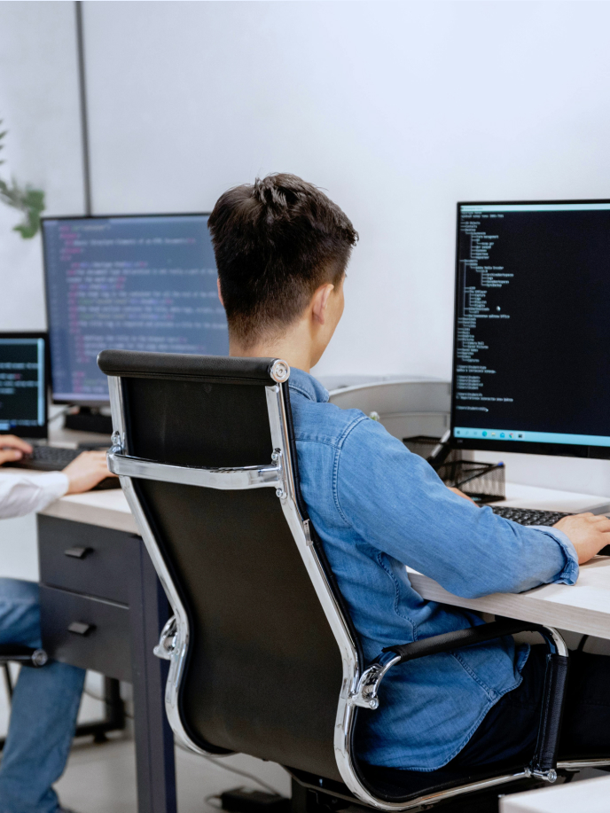 A person is seated at a desk in front of multiple computer monitors displaying code