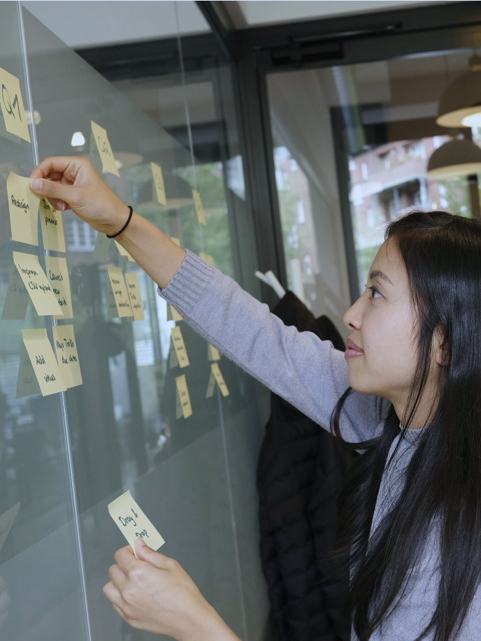 A person is adding sticky notes to a glass wall