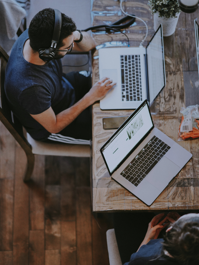 Two people are working on laptops at a wooden table