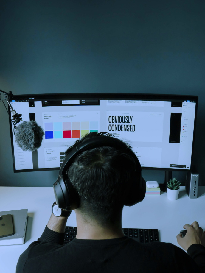 A person wearing headphones is looking at a computer screen with design elements and color palettes.